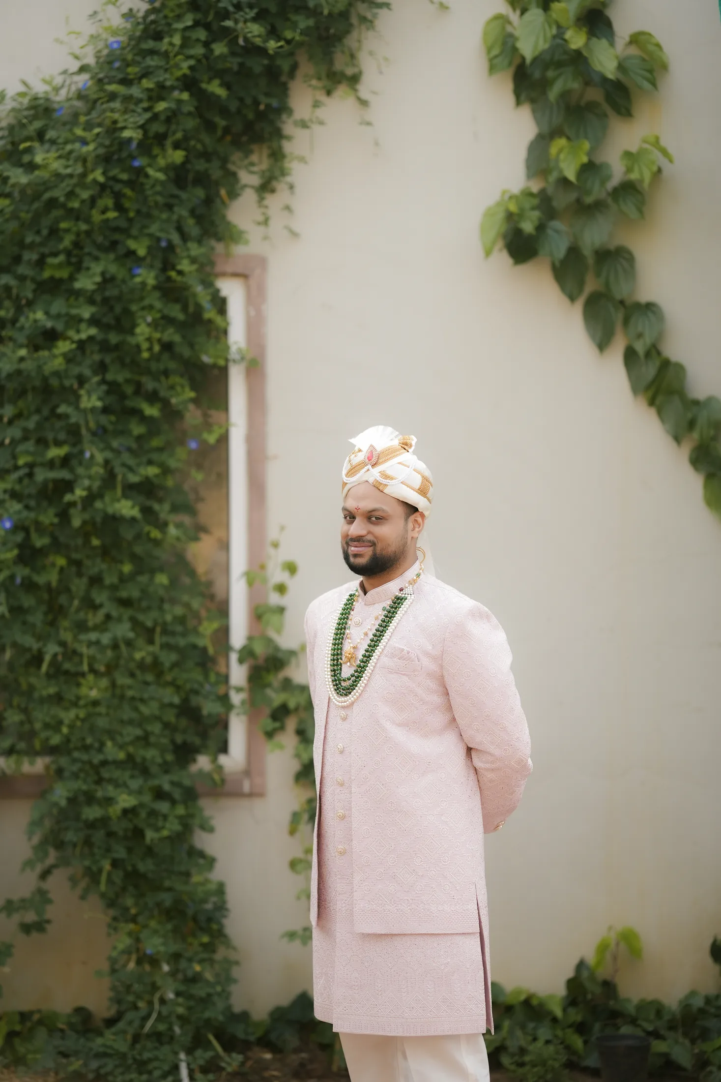 Groom standing against an ivy covered wall